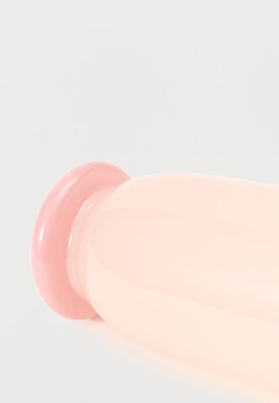 Κοντινό πλάνο ενός απαλού ροζ και μπεζ αντικειμένου από σιλικόνη με στρογγυλεμένο άκρο και φαρδιά βάση, τοποθετημένο πάνω σε απλό ανοιχτό φόντο.