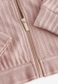 Rosa Strickjacke mit gerippter Textur, ausgestattet mit einem goldenen Reißverschluss und elastischen Bündchen. Logo-Detail am Saum, weicher Stoff.
