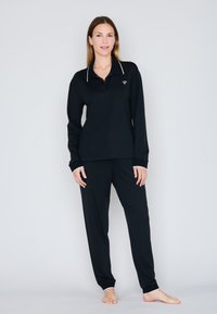 Zwarte lange mouw polo met witte accenten, gecombineerd met zwarte broek. Gladde stof, relaxte pasvorm en elastische manchetten bij de polsen en enkels.