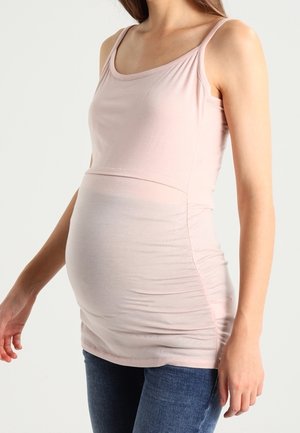 Lyserød graviditetstanktop med tynde stropper, med tætsiddende pasform, rynkede sider og blødt, elastisk stof. Kombineret med mørke denimjeans.