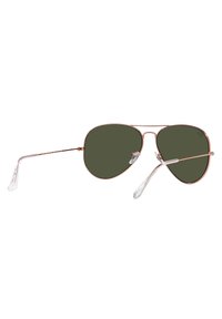 Occhiali da sole aviator con lenti verdi, montatura in metallo dorato e punte in plastica trasparente. Design minimalista con linee curve e finitura lucida.