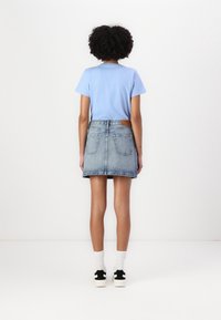 Light blue t-shirt with short sleeves paired with a dark blue denim skirt. The outfit includes white socks and black-accented sneakers.