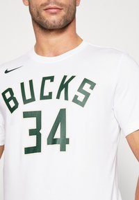 Hvid kortærmet t-shirt med grøn "BUCKS" tekst og "34" på forsiden, samt et sort Nike-logo på venstre skulder.