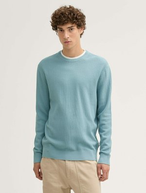 Hellblauer strukturierter Strickpullover mit rundem Ausschnitt und gerippten Bündchen. Kombiniert mit beigen Hosen. Flaches, lässiges Design, keine Muster.