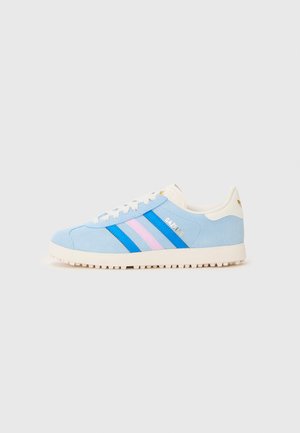 Lyseblå semsket sneakers med hvit gummisåle, med blå og rosa diagonale striper, og "GAZELLE"-logo i gull.