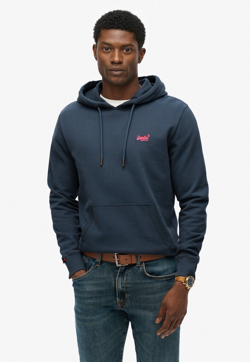 Navy blauwe hoodie van katoenmix met een voorvak, trekkoordcapuchon en klein roze logo op de borst. Gecombineerd met spijkerbroek.