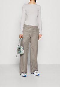 Lange mouwen grijze top, lichte stof; beige gestreepte wijde broekspijpen; iriserende kleine handtas; witte en blauwe sportschoenen.