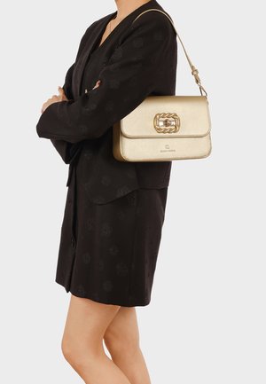 Donna che indossa un abito blazer nero testurizzato con una borsa a tracolla dorata con una grande fibbia decorativa.