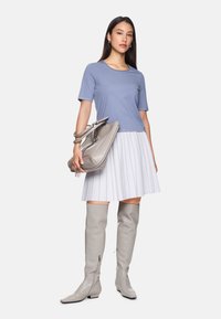 Helles blaues Kurzarmoberteil, weißer gefältelter Rock, graue Stiefel über dem Knie und eine graue Handtasche mit Fransen und metallischen Akzenten.