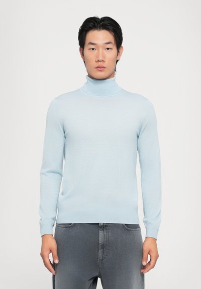 Suéter de cuello alto azul claro hecho de una tela suave, con mangas largas y un diseño ajustado, combinado con pantalones de mezclilla grises.