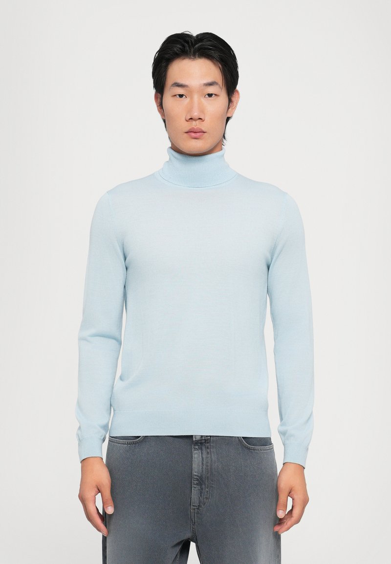 Lys blå høyhalset genser laget av glatt stoff, med lange ermer og en tettsittende design, sammen med grå denimplagg.