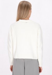 Biały sweter wykonany na drutach z prążkowanym dołem i mankietami. Posiada okrągły dekolt i luźny krój. Gładka tekstura z minimalnymi detalami.