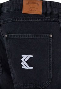 Pantaloni in denim nero con etichetta in pelle con scritto "KARL KANI" e logo ricamato bianco sulla tasca posteriore. Accenti metallici presenti.