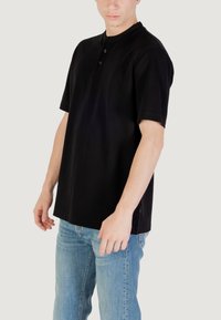 Camiseta henley de manga corta negra con tres botones en el escote, fabricada en tejido suave, con un corte relajado y costuras laterales visibles.