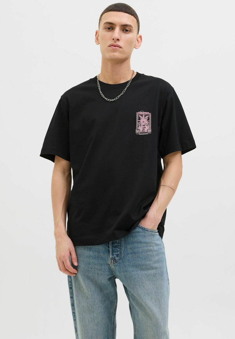 Sort bomulds T-shirt med et pink grafisk design på brystlommen. Kombineret med lyseblå denimjeans. Enkel rund hals, afslappet pasform.