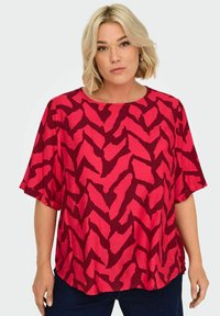 Piros és rózsaszín, rövid ujjú felső, zig-zag mintázattal, könnyű anyagból, laza fazonnal és kerek nyakkivágással.