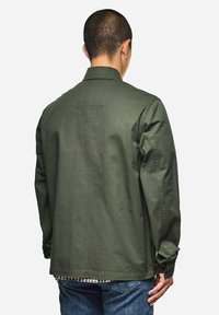 Olivgrüne leichte Jacke mit lockerer Passform, langen Ärmeln und geradem Saum. Verfügt über eine Rückenpasse und Knopfdetails an den Manschetten.