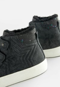 Czarne buty typu high-top z teksturą w gwiazdy, puszyste czarne wykończenie oraz wielokolorowe akcenty w formie gwiazdek przy kostce; biała gumowa podeszwa.