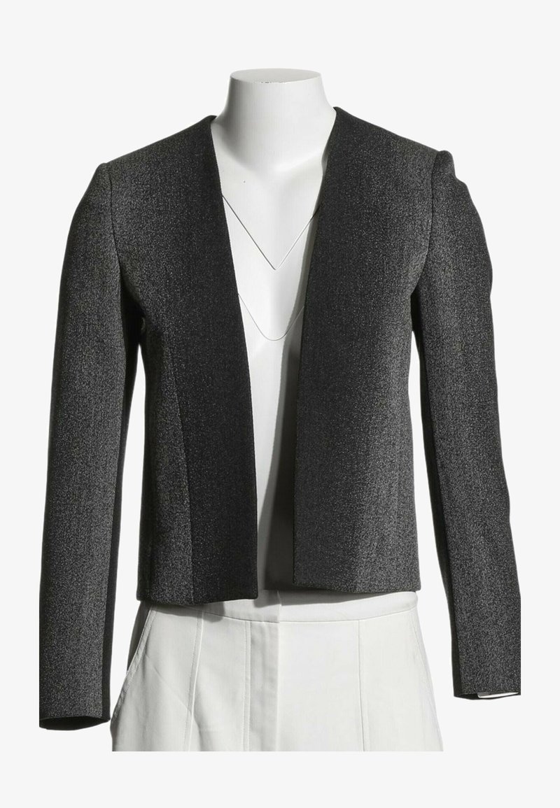 Blazer gris foncé texturé à ouverture frontale avec manches longues sur un torse de mannequin blanc portant un pantalon blanc.