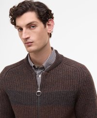 Cardigan zippé côtelé marron et gris avec un col rond, présentant des motifs de rayures horizontales et une fermeture éclair métallique. Porté au-dessus d'une chemise à carreaux.