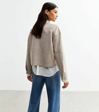 Afgekorte beige suède jas met een overhemd eronder, met lange mouwen en knoopdetails, gecombineerd met losse blauwe denimjeans.