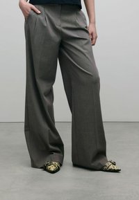 Grijze wijde broek met plooien, gecombineerd met gestreepte zwart en beige schoenen. De stof is glad met een subtiele textuur.