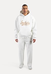 Weißes Hoodie- und Jogginghosen-Set mit einem großen goldenen "Smilodox"-Logo. Der Stoff scheint weich und mit einer glatten Textur zu sein.