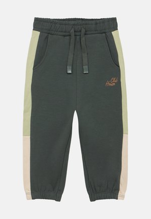 Pantalon de survêtement vert foncé avec une ceinture élastique, des panneaux latéraux contrastants vert clair et beige, et un logo "Club House" en orange.