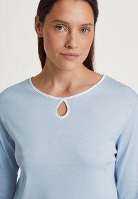 Lichtblauw langwerpig t-shirt met een ronde halslijn en een sleufje, accentueert met een witte rand. Zachte, gladde stoftextuur.