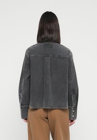 Black denim jacket with a relaxed fit, featuring a back vent, sturdy stitching, and buttoned cuffs. Textured fabric adds visual interest.