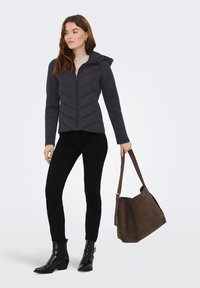 Γκρι καπιτονέ μπουφάν με κουκούλα, με σχέδιο σε σχήμα V, συνδυασμένο με στενά μαύρα τζιν και λαμπερά μαύρα μποτάκια αστραγάλου. Καφέ τσάντα.