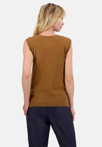 Pull sans manches marron en matière douce, avec un col rond et un ourlet côtelé, associé à un pantalon bleu marine.