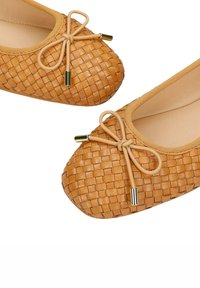 Beige geweven leren ballerina's met strikaccenten en gouden metalen punten op een witte achtergrond.