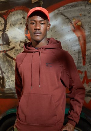 Maronfarvet Nike hoodie med kængurulomme, snore samt logo på brystet. Lys rød cap komplementerer outfittet. Tekstureret stof.