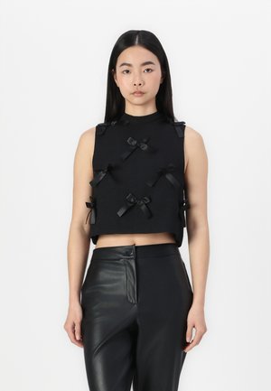 Top court noir en tissu texturé, orné de plusieurs petits nœuds noirs en accent à l'avant. Assorti avec un pantalon noir ajusté.