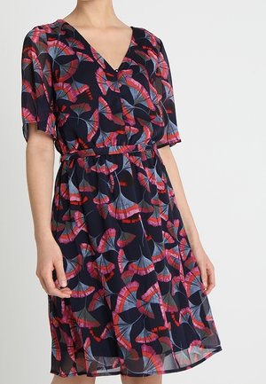 Sukienka w kwiaty z granatowej tkaniny ozdobiona czerwonymi i niebieskimi liśćmi. Dekolt w serek, krótkie rękawy, taliowana, z zwiewnym dołem.