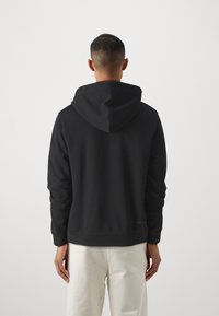 Černá mikina s kapucí vyrobená z měkkého materiálu, s velkou kapucí, dlouhými rukávy a žebrovaným lemem. Minimalistický design, bez viditelných log a vzorů.