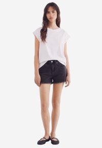 Hvid kortærmet top med hulmønster, parret med sorte denimshorts og sorte flade sko. Enkelt design, afslappet pasform og let tekstur.