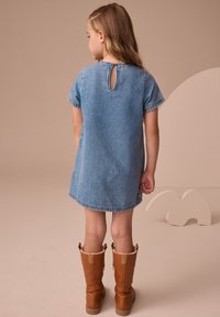 Mėlyna džinsinė suknelė, trumpomis rankovėmis, suapvalinta nugara su plyšiu, siūtu apvadu. Derinama su rudu ilgaauliais batais, išklotais avies vilna ir užsegamais mygtukais.