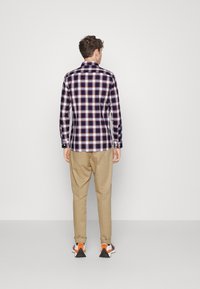 Camicia a quadri nei colori navy, bianco e ruggine, con polsini abbottonati e colletto. Abbinata a pantaloni beige e sneakers multicolori.