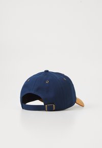 Navy blue cap with a brown peak, made from sturdy fabric. Features eyelets for ventilation and an adjustable strap at the back.