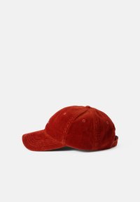 Punainen corduroy-baseball-lippu, jossa on kaareva lippa, säädettävä hihna takana ja pieniä ilmanvaihtorei'itä kruunussa.