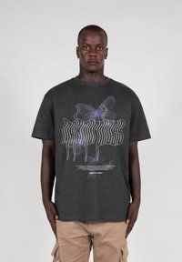 Camiseta de algodón gris con un gráfico de mariposa blanca y morada y texto estilizado en el frente, con un cuello redondo estándar y mangas cortas.