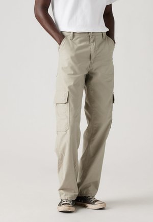 Pantaloni cargo beige con tasche laterali, realizzati in tessuto morbido. Vestibilità ampia, design a gamba dritta, abbinati a sneaker nere.
