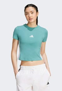 Teal, kortärmad crop top i mjukt tyg, med en vit Adidas-logotyp på bröstet och kontrasterande vita sidränder.