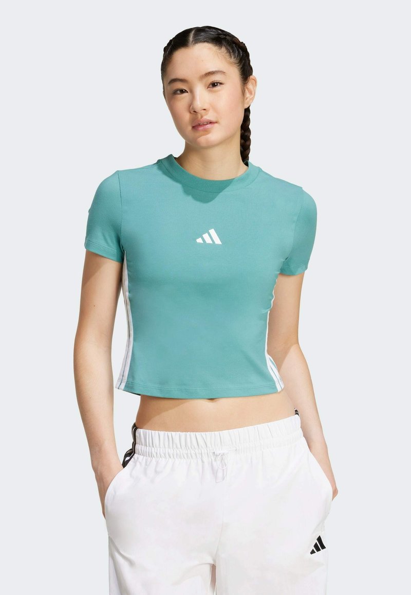 Teal, kortärmad crop top i mjukt tyg, med en vit Adidas-logotyp på bröstet och kontrasterande vita sidränder.