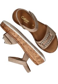 Beige suède sandalen met een kurken platform en een witte rubberen zool. Voorzien van een band met metalen accenten en een verstelbare achterkant voor een goede pasvorm.
