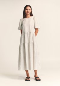 Robe midi grise à rayures avec manches courtes bouffantes, taille froncée et silhouette fluide, portée avec des sandales plates noires.