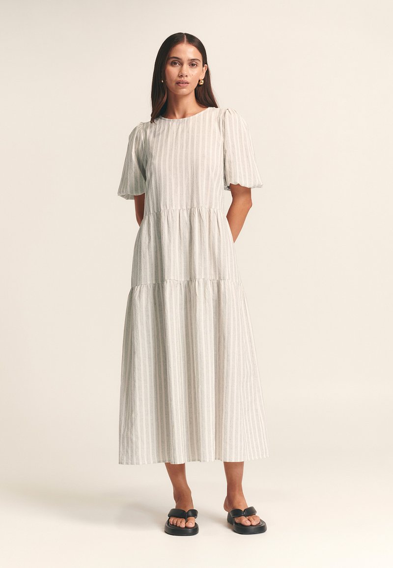 Robe midi grise à rayures avec manches courtes bouffantes, taille froncée et silhouette fluide, portée avec des sandales plates noires.