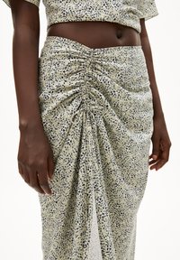 Gerimpelde rok van lichtgroene stof met een marineblauw en crèmekleurig gesprenkeld patroon. Middenlange stijl met een zijsplit en geplooide details bij de taille.